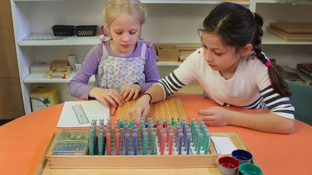 2 Little girls play with different coloured beads in vials