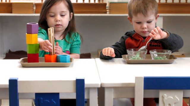 A little boy and girl use spoons and tongs to pick up toys at a table