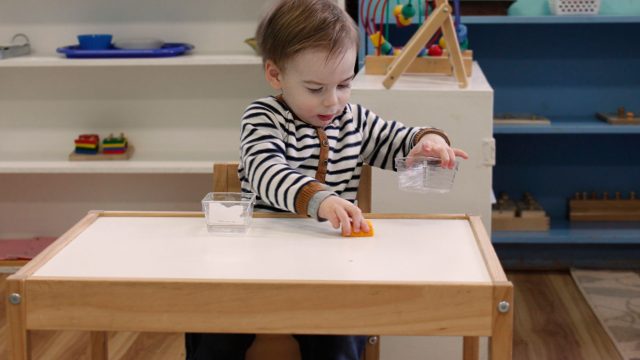 A little boy sitting at a table playing with clear containers