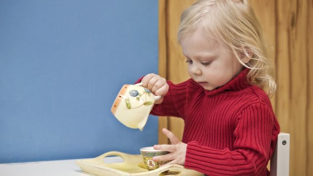 A little girl pretends to pour tea into a cup