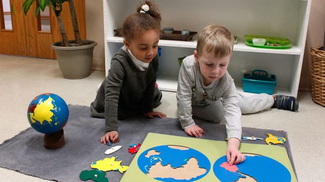 A little girl and boy sit on the floor putting together a puzzle of the earth