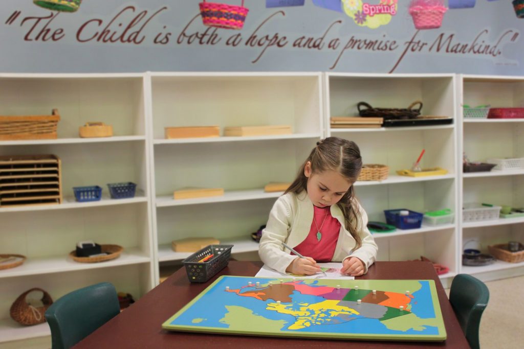 A little girl works on a worksheet in front of a map of Canada