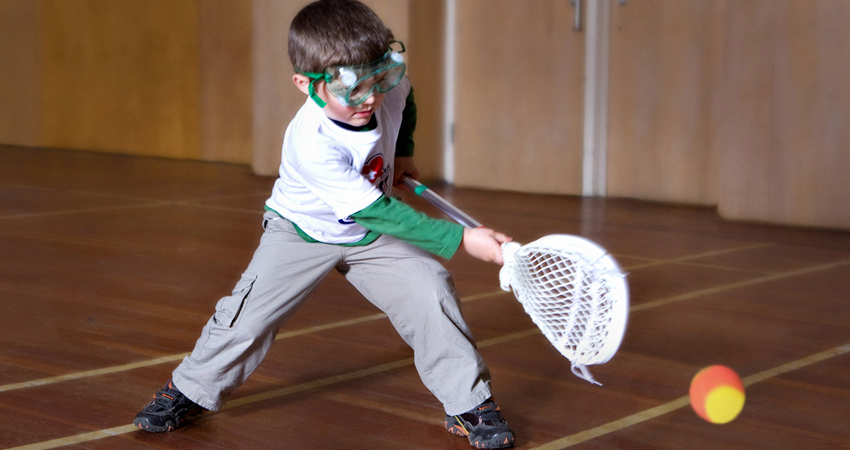 A little boy in goggles playing lacrosse
