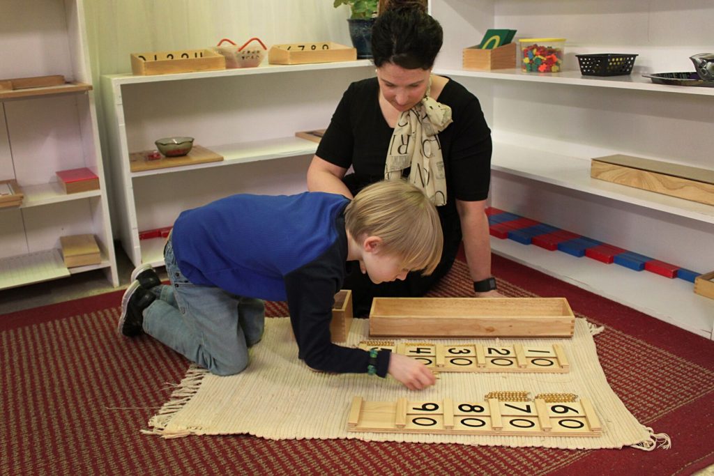 Teacher sitting on the floor with a little boy, using a wooden toy with numbers