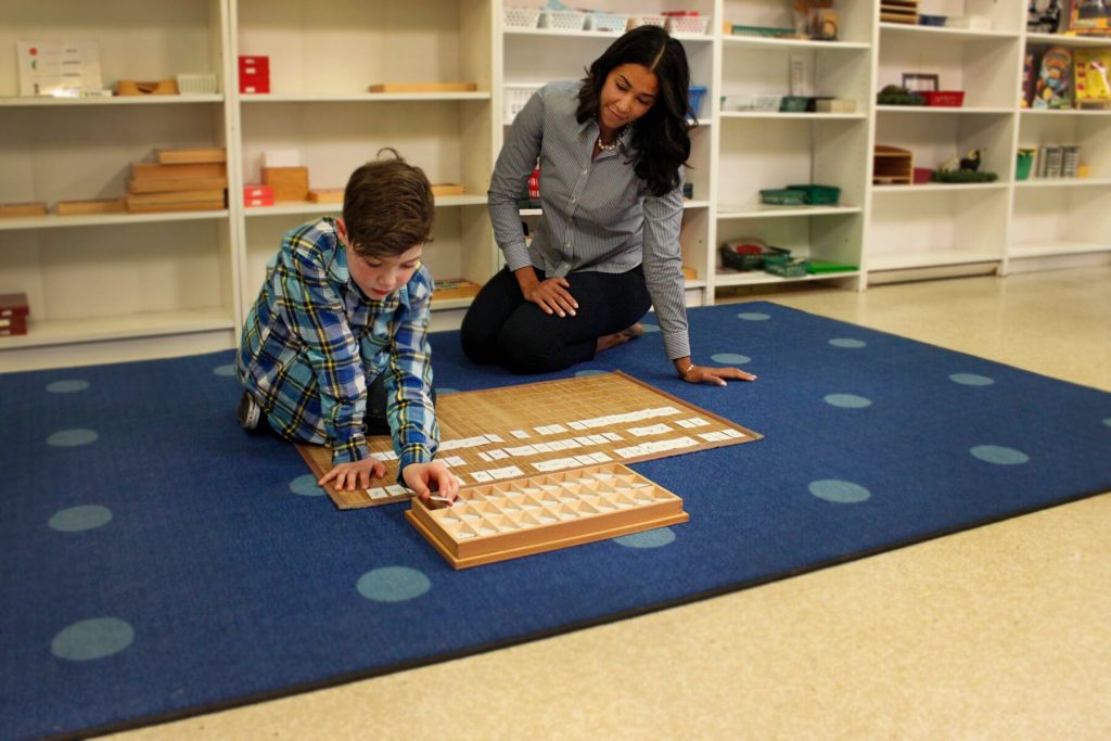 A little boy and his teacher sit on the floor playing with toys