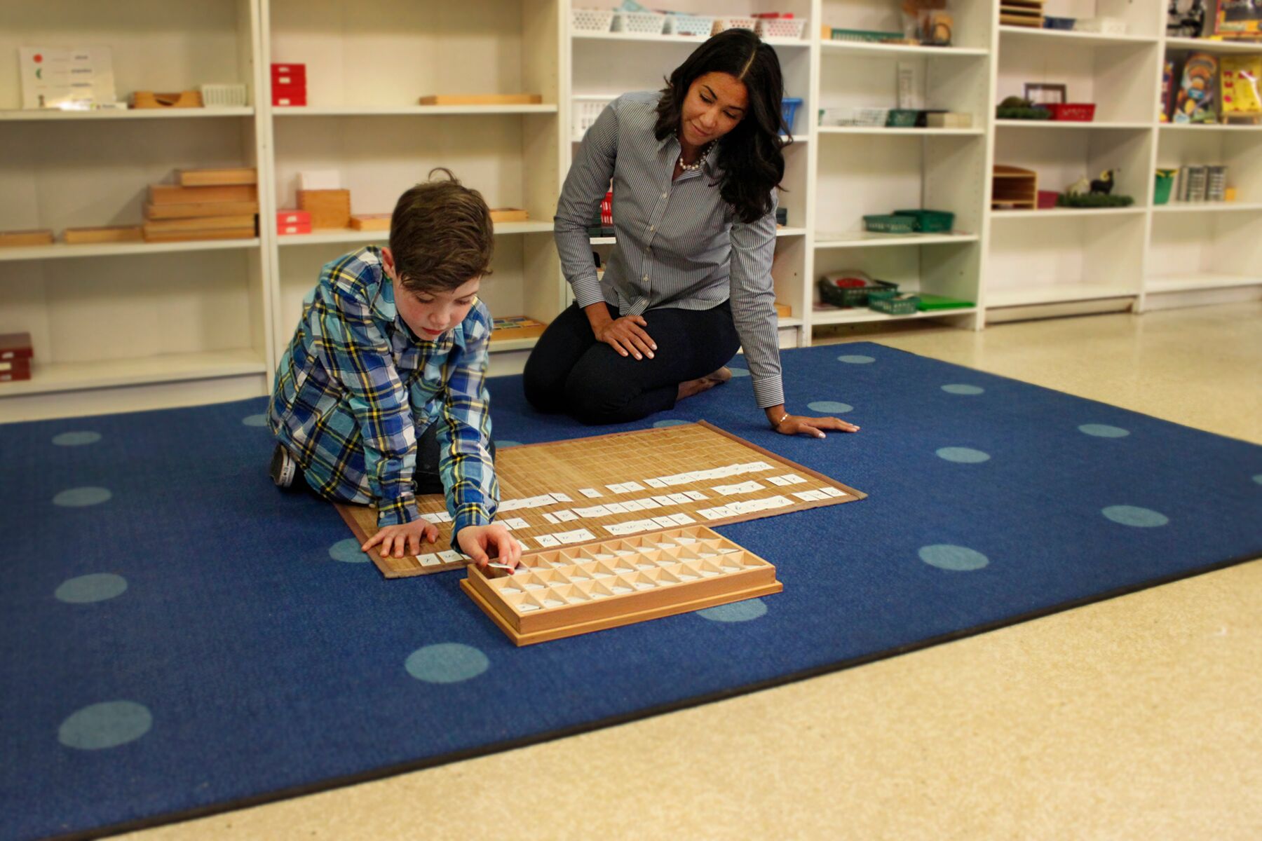 A little boy and his teacher sit on the floor playing with toys