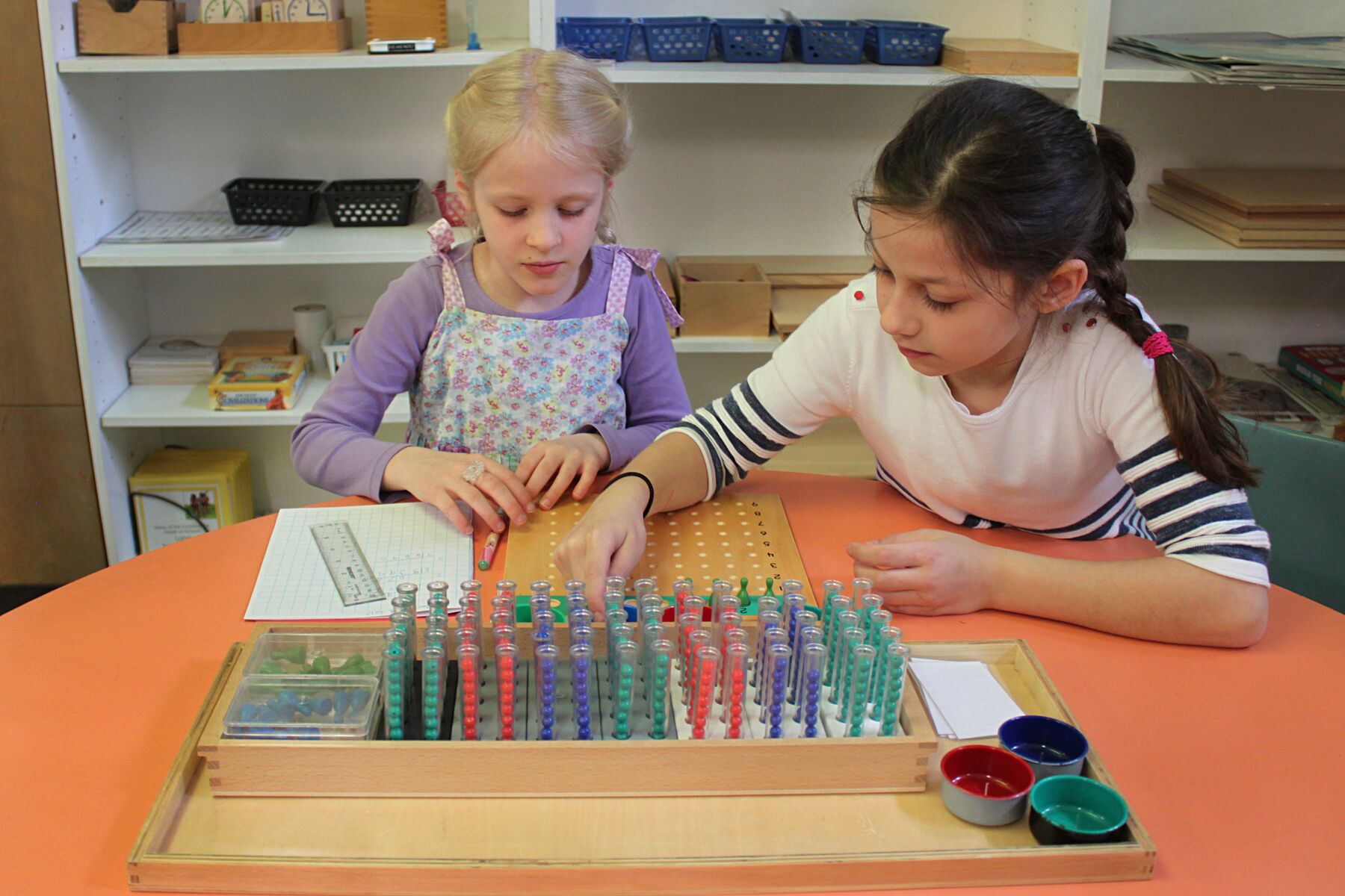 2 Little girls play with different coloured beads in vials