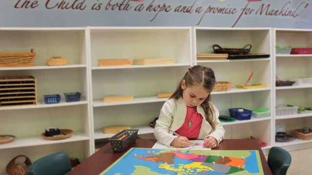 A little girl works on a worksheet in front of a map of Canada