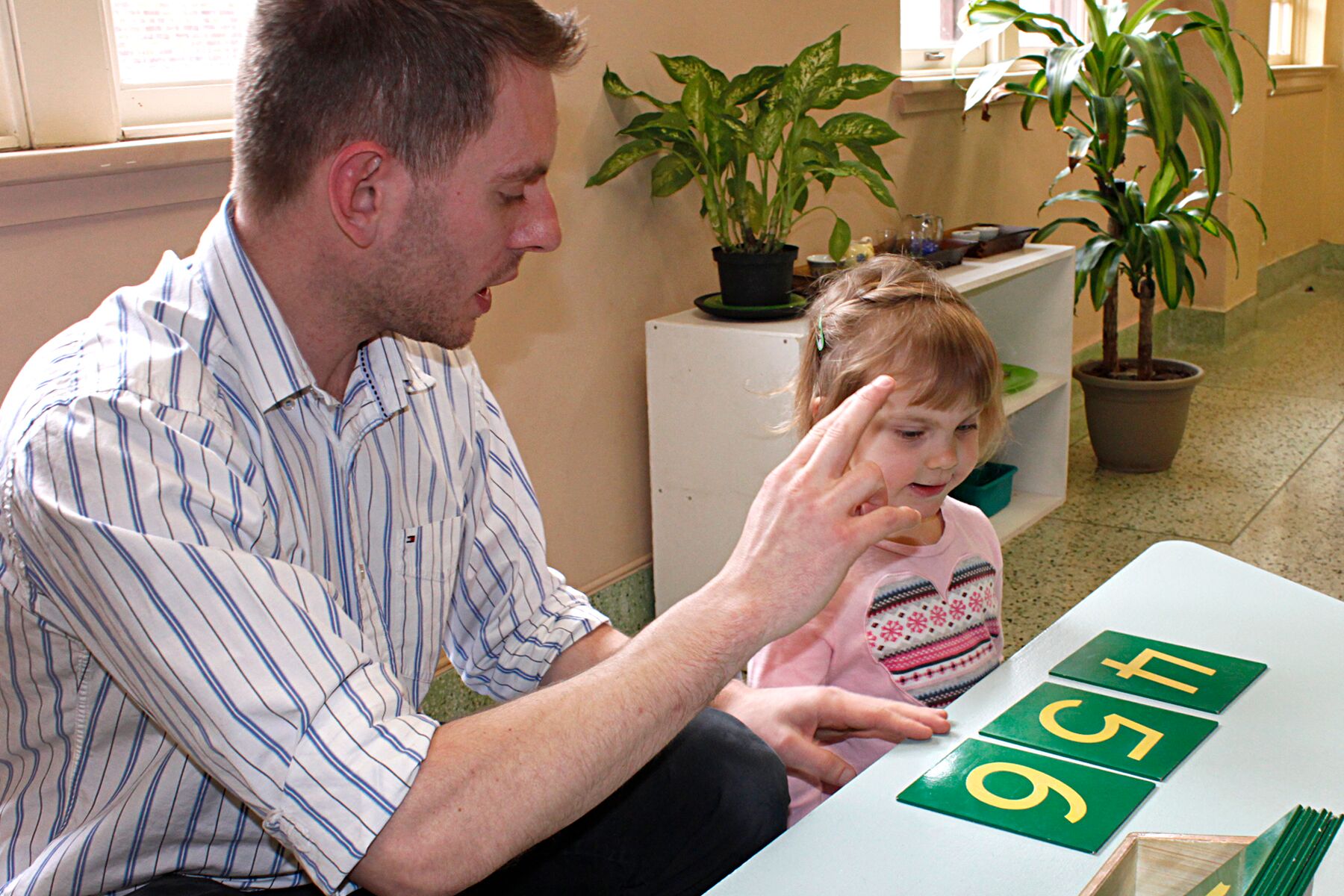 A teacher teaching numbers to a little girl using flash cards